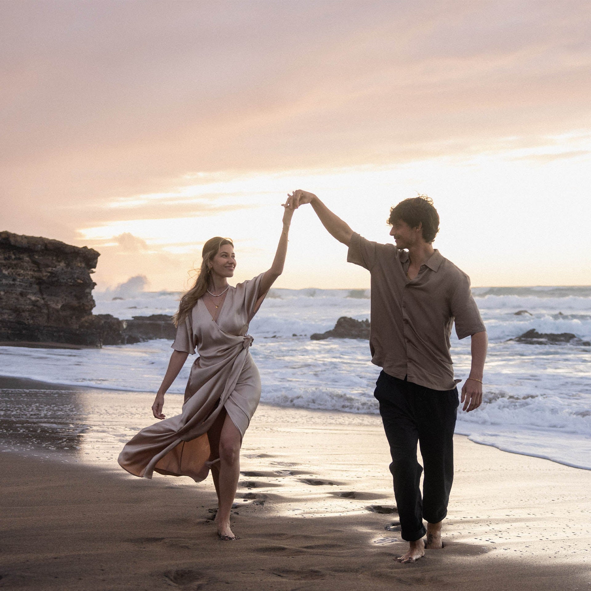 Paar tanzt barfuß am Strand, Frau mit PURELEI Anxiety Lovely Ring aus Muschelperlen und Herz in warmem Licht.