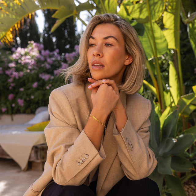 Elegantes, goldenes Armband von PURELEI, getragen in tropischer Umgebung.