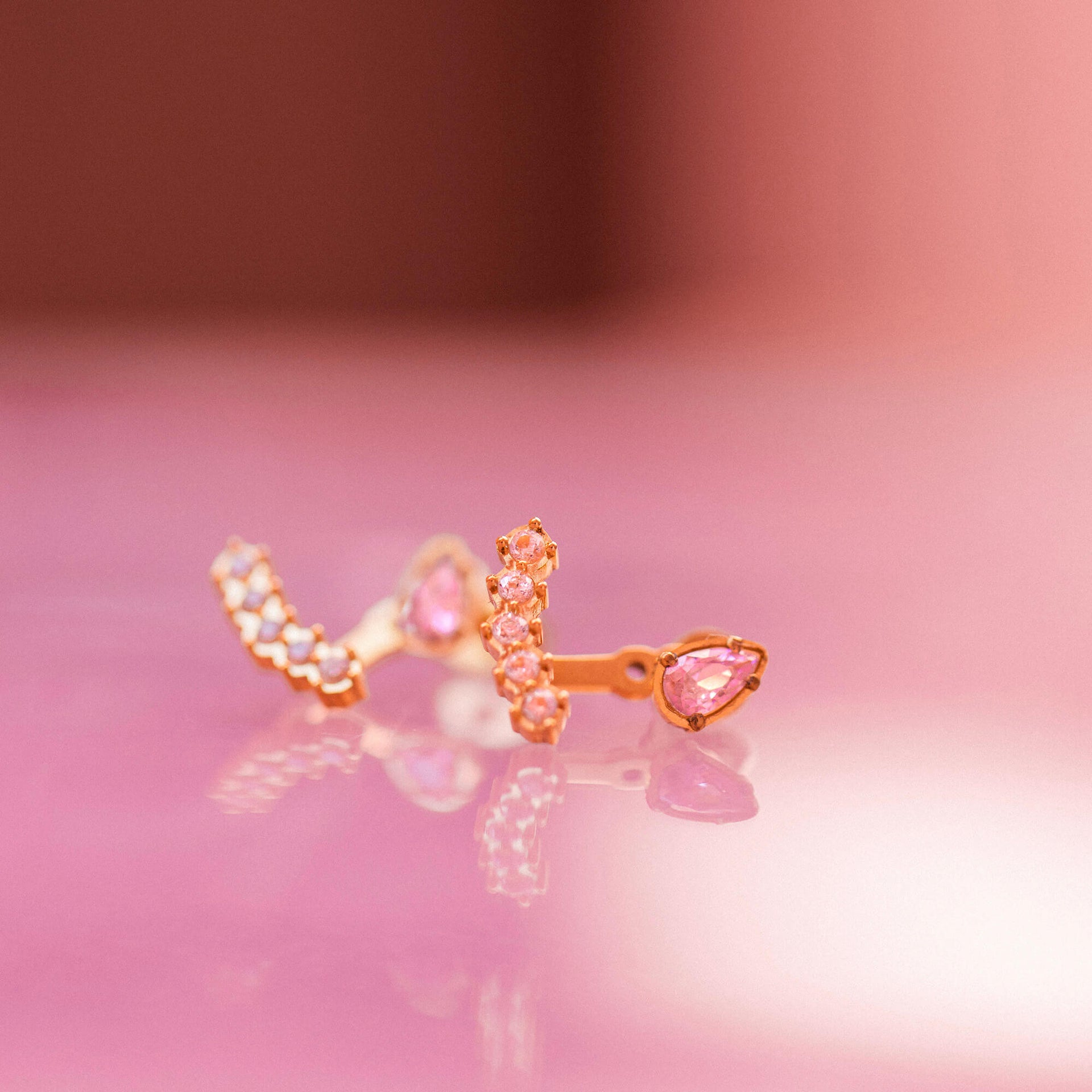 Adore Ohrringe aus rosévergoldetem Edelstahl mit rosa und weißen Zirkonia, elegant auf rosa Hintergrund, PURELEI