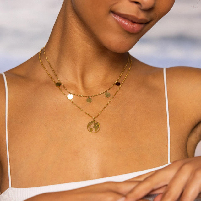 Zwei goldene Ketten mit runden Anhängern und Weltmotiv, getragen von PURELEI.