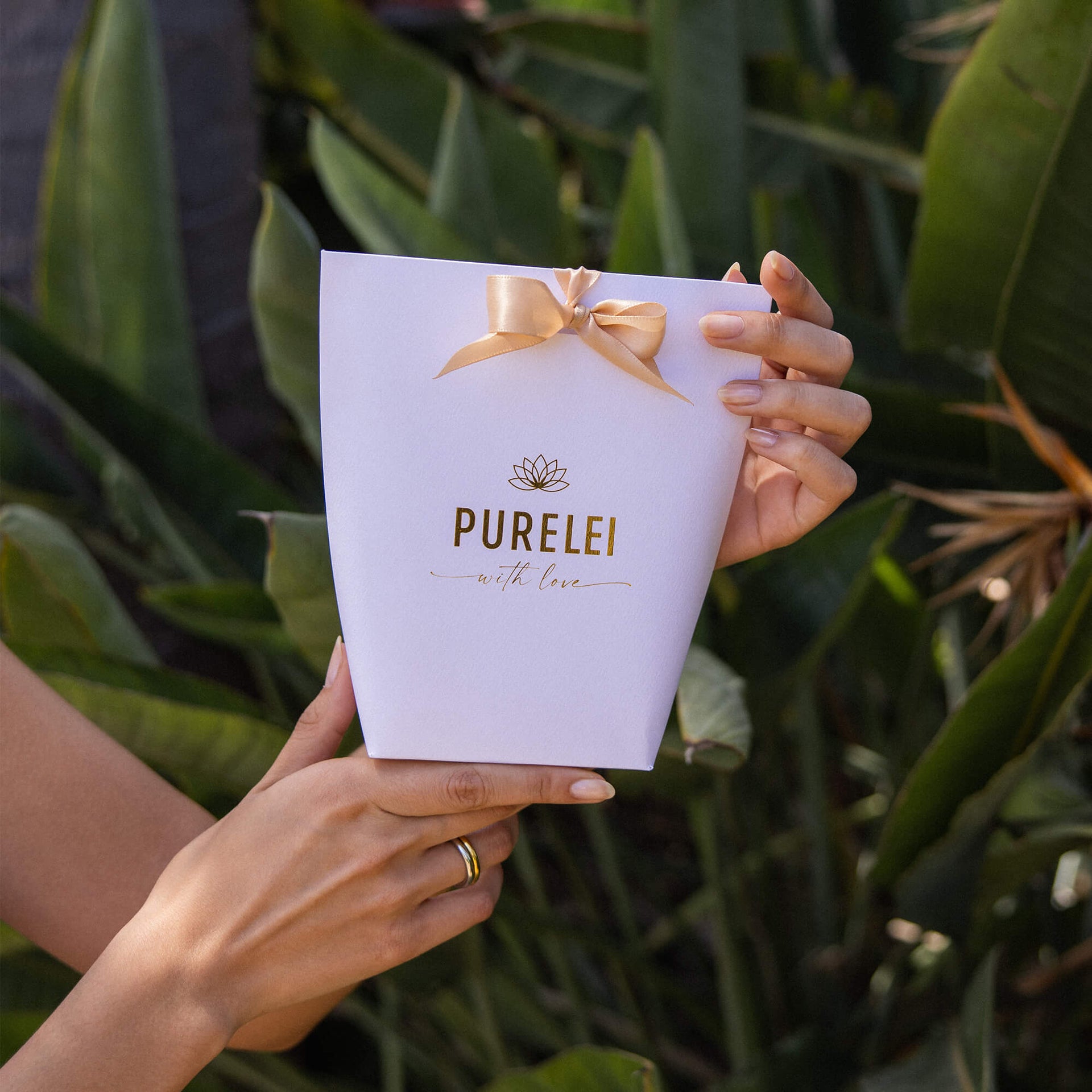 PURELEI Geschenkverpackung aus weißem Papier mit Goldprägung und Schleife, elegant und feminin inszeniert.