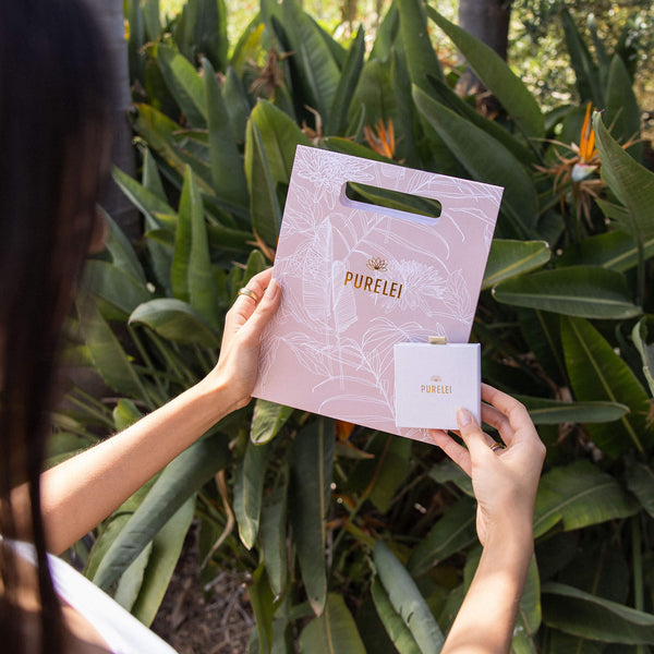 Zarte PURELEI Geschenkverpackung in Rosa mit botanischem Design, umgeben von tropischen Pflanzen.