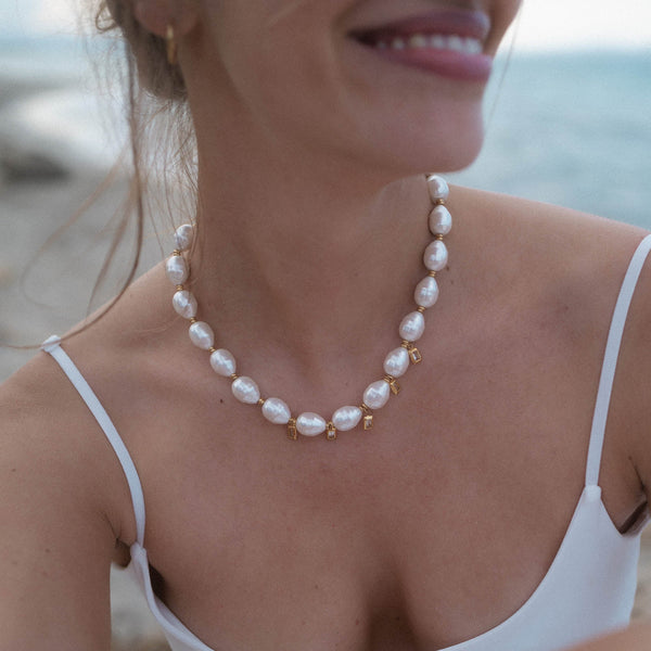 Perlenkette in Weiß mit goldenen Akzenten, getragen am Strand – PURELEI Eleganz.