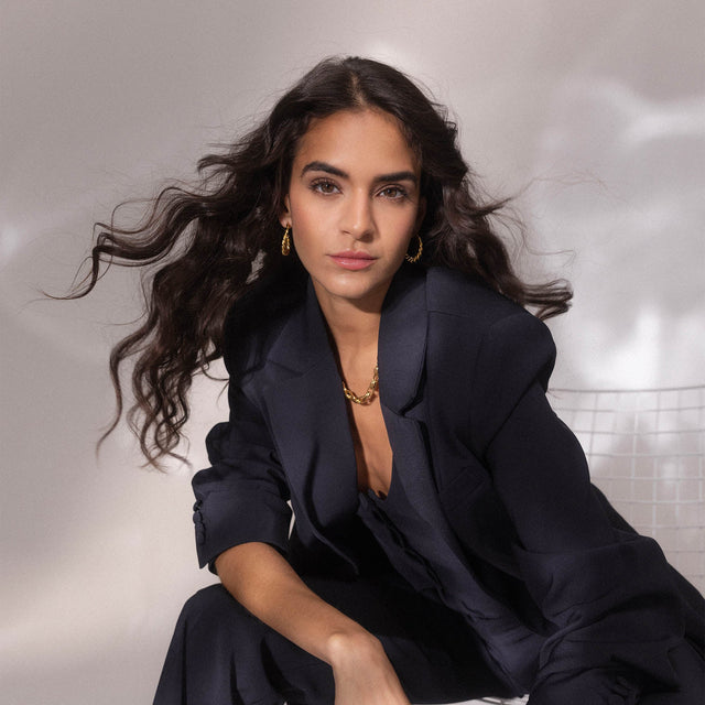 Elegante Frau mit lockigem Haar, trägt PURELEI Schmuck in einem stilvollen, dunklen Outfit.