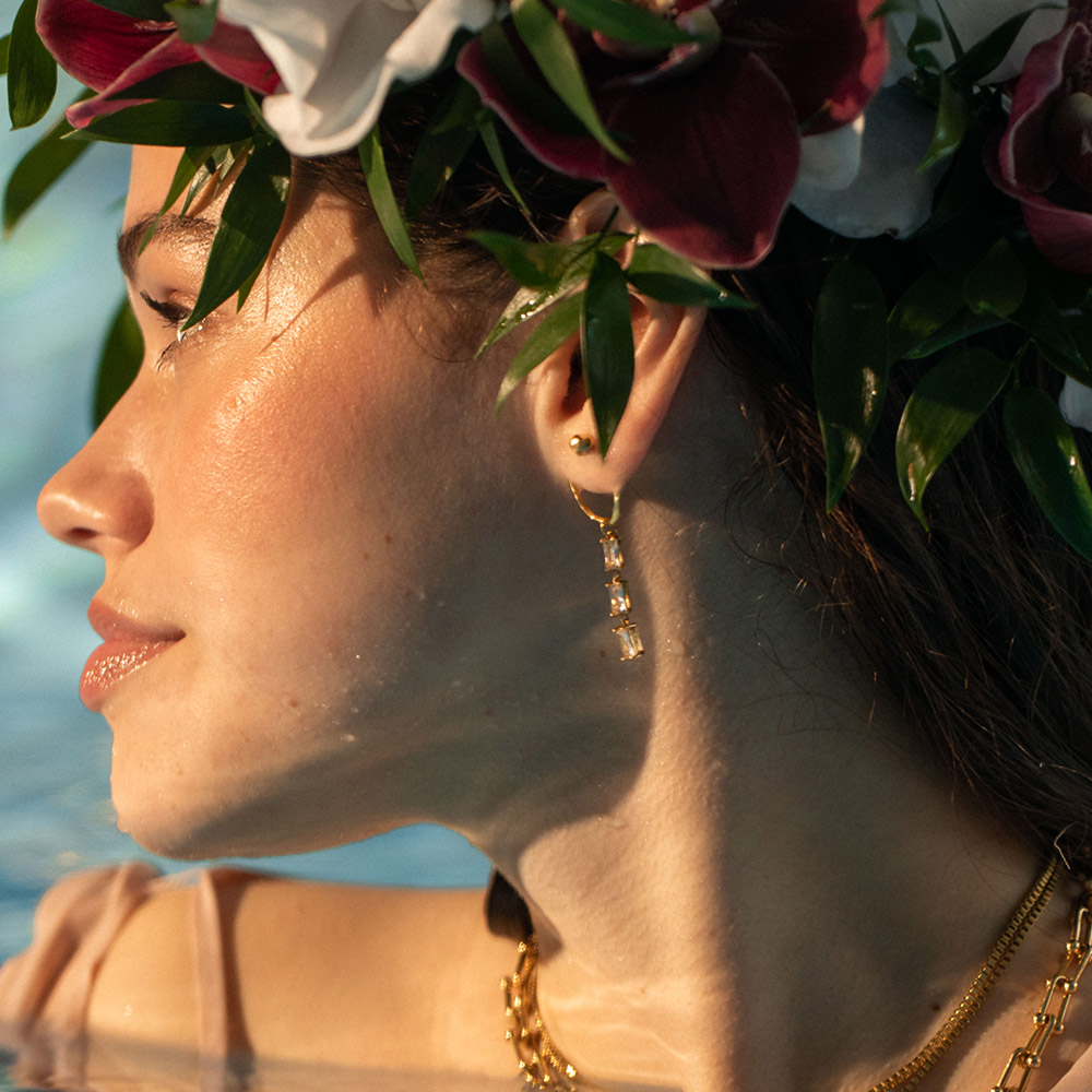 Elua Ohrringe aus 18K Gold mit funkelnden Zirkonia und Perle, getragen im warmen Sonnenlicht von PURELEI.