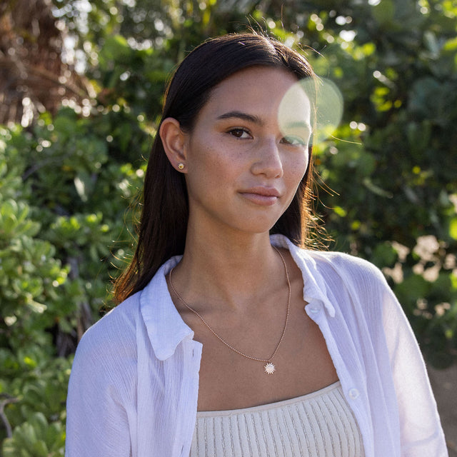 Goldene Sonnensonnenkette von PURELEI, getragen in tropischer Umgebung.
