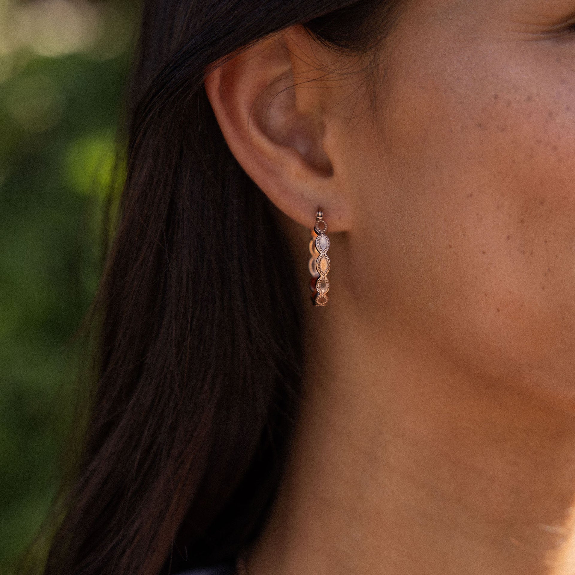 Roségoldene Ohrringe mit geschwungenem Design, getragen in natürlicher Umgebung – PURELEI.