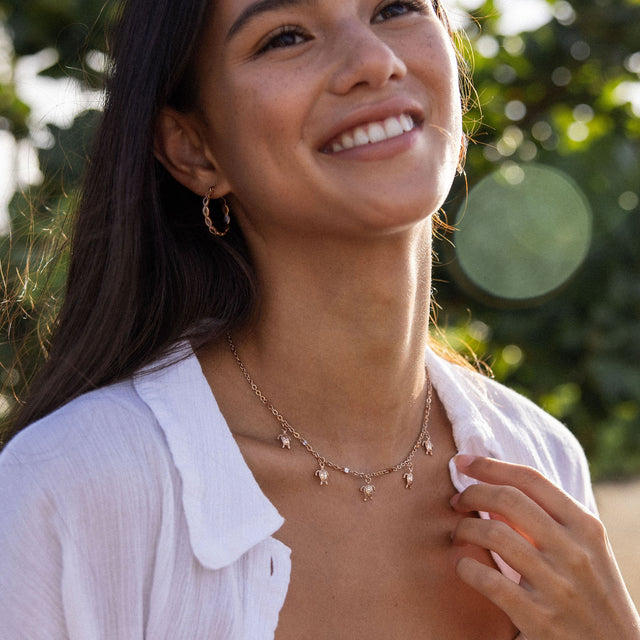Roségoldene Kette mit Anhängern, getragen von einer lächelnden Frau, PURELEI.