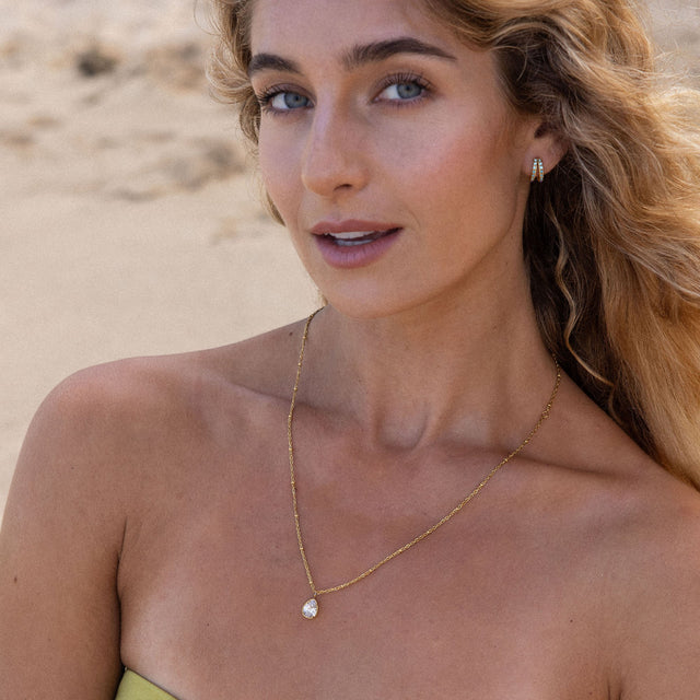 PURELEI Felice Kette mit vergoldeter Edelstahlkette und weißem Zirkonia-Tropfen vor Strandkulisse getragen