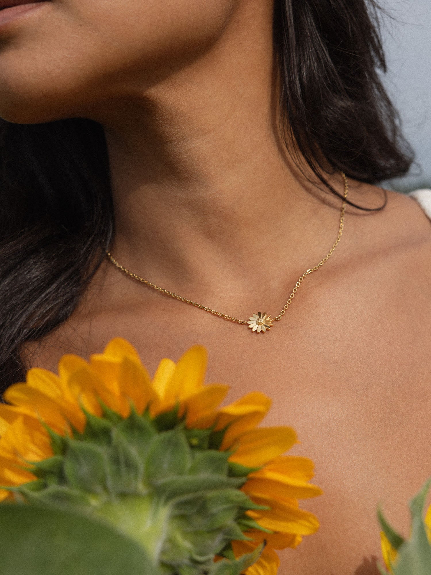 Goldene Kette mit Blumenanhänger, getragen mit Sonnenblumen im Hintergrund – PURELEI.