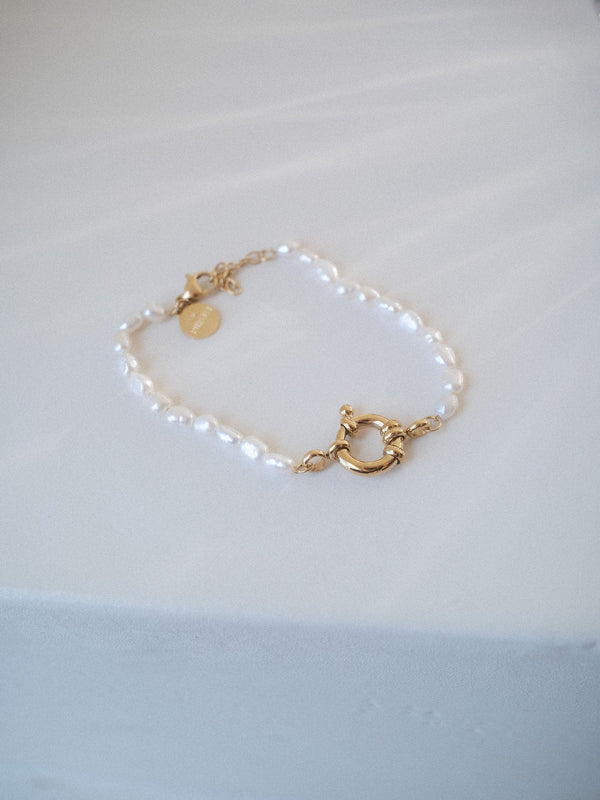 Charm Armband mit Perlen von PURELEI aus vergoldetem Edelstahl und Süßwasserperlen, elegant auf hellem Stoff liegend.