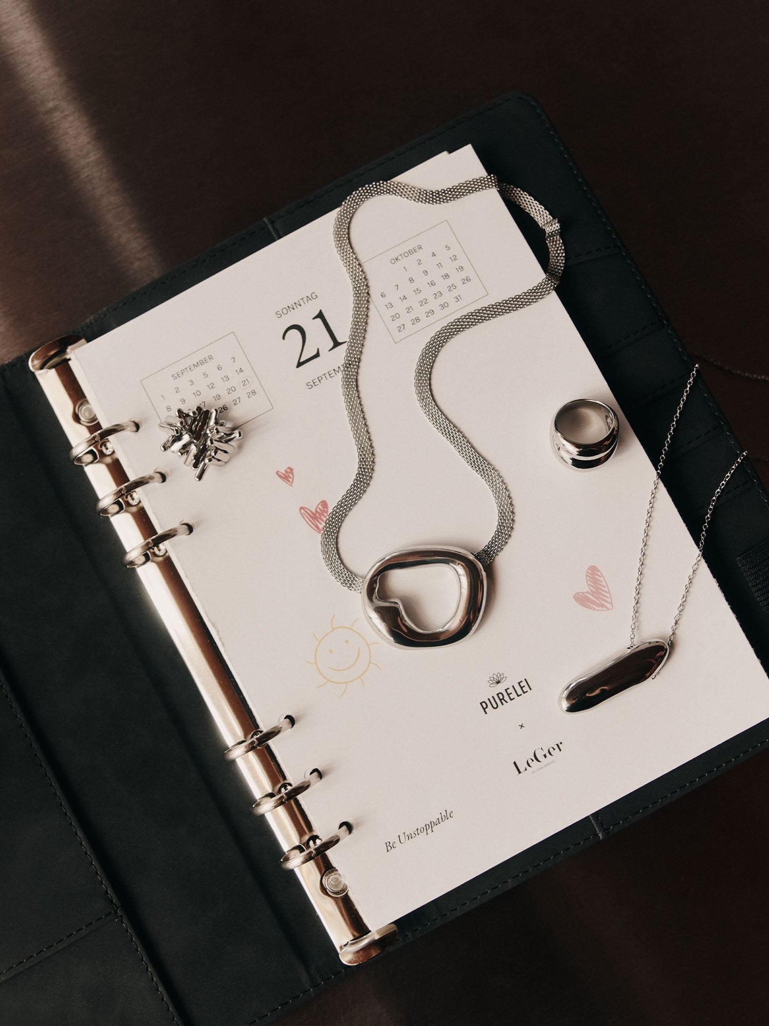 Silberne PURELEI Kette mit organischem Anhänger auf einem Kalenderblatt.