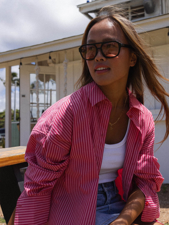 Frau in gestreifter, roter Bluse mit PURELEI Schmuck, lächelnd im Sonnenlicht.