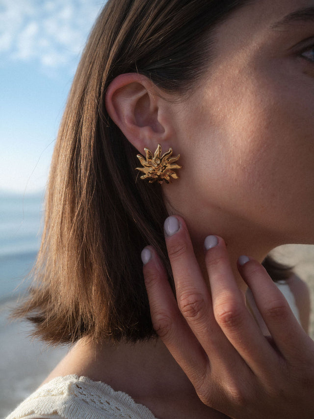 Iconic Sun Ohrringe von PURELEI, goldene Edelstahl-Ohrringe mit strukturiertem Sonnenmotiv im natürlichen Meereslicht