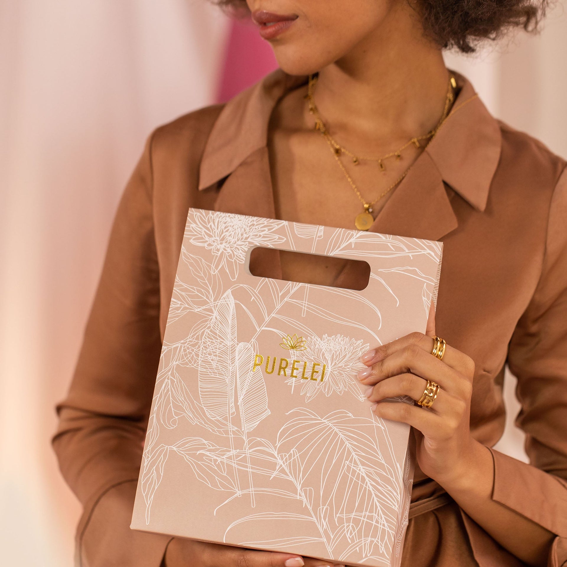Elegante PURELEI Geschenkverpackung in sanften Erdtönen mit floralem Design, gehalten von einer Frau.