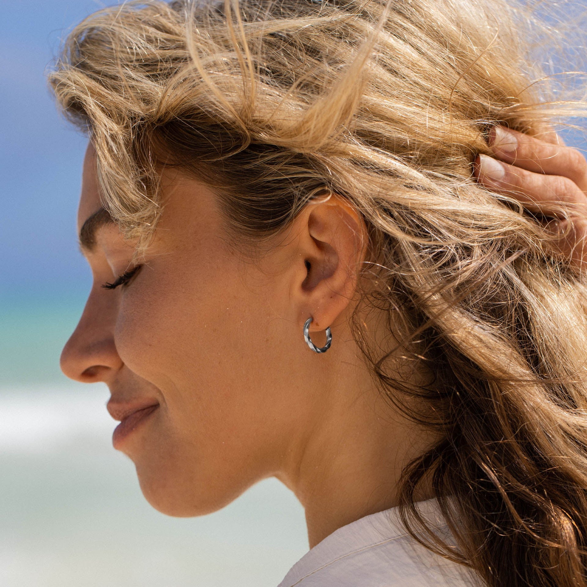 PURELEI Kelani Ohrringe aus silbernen Creolen mit twisted Design, getragen am Strand, beachy und elegant.