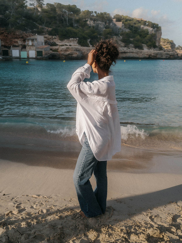 PURELEI Breeze Bluse aus weißer Baumwolle mit dezenter Stickerei, luftig und beachy an Meeresufer getragen