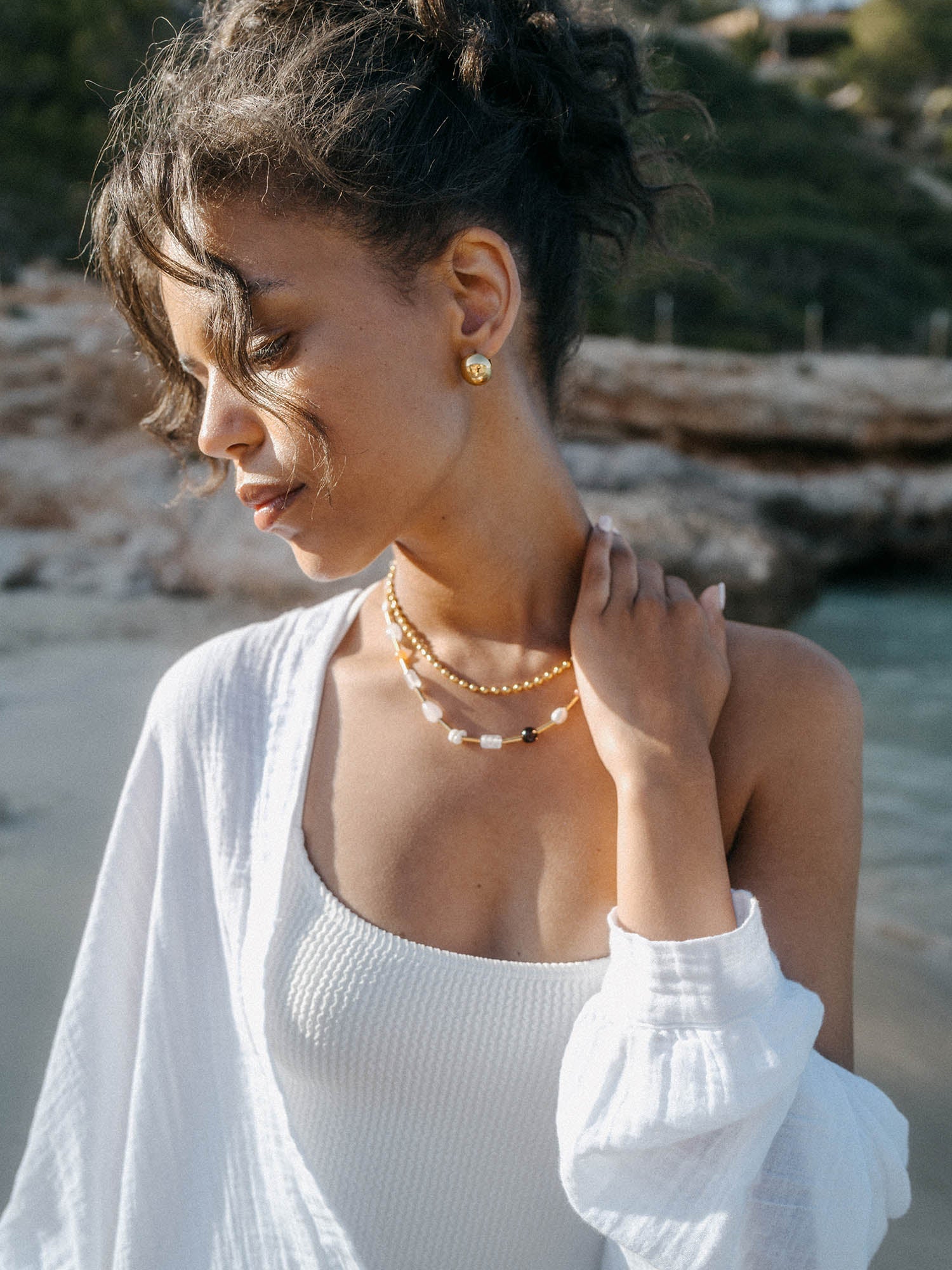 Zarte PURELEI Kette mit Perlen und schwarzem Detail, getragen in sonniger Strandatmosphäre.