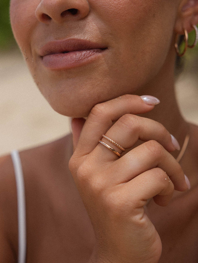Zarte, roségoldene Ringe von PURELEI an einer Hand, umgeben von warmem Licht.