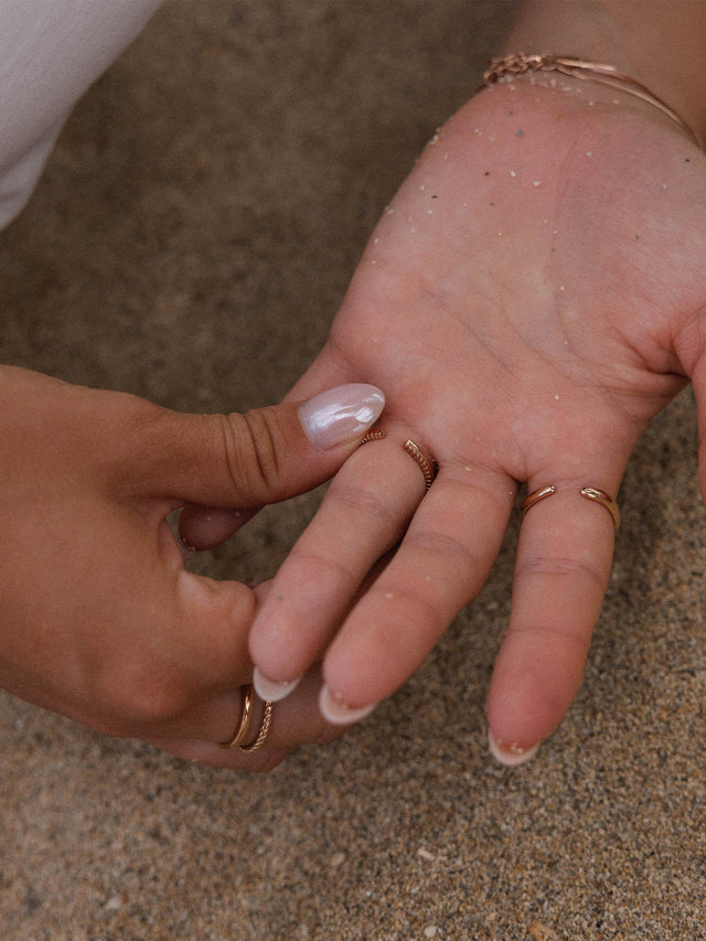 Roségoldene Ringe auf einer Hand, umgeben von Sand – PURELEI Eleganz und Natürlichkeit.