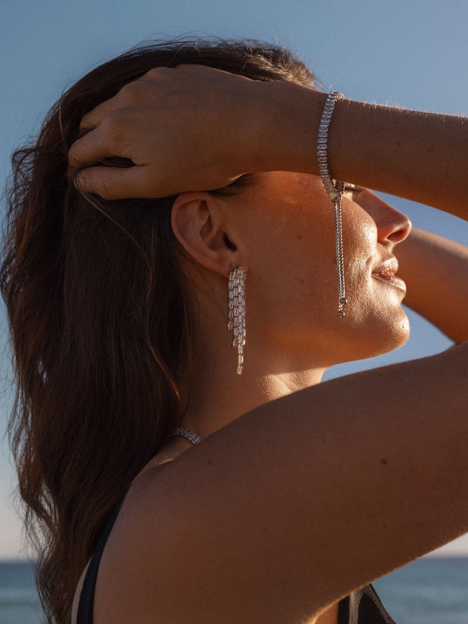 Silberne Ohrringe und Armband von PURELEI, elegant und funkelnd, am Strand getragen.