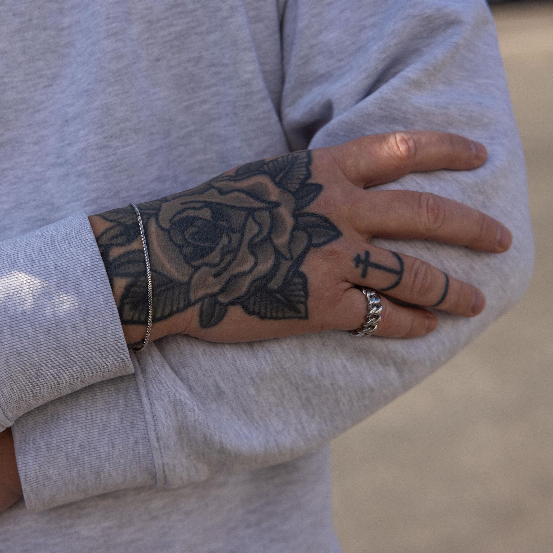 Silbernes Armband und Ring von PURELEI, getragen mit tätowierter Hand, lässige Stimmung.