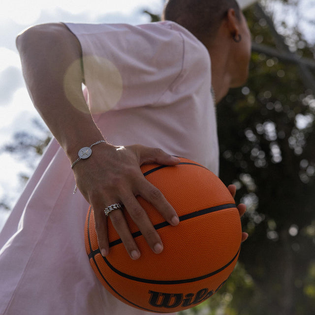 Silberne PURELEI Armbanduhr und Ring, sportlich am Basketball gehalten, mit natürlichem Licht.