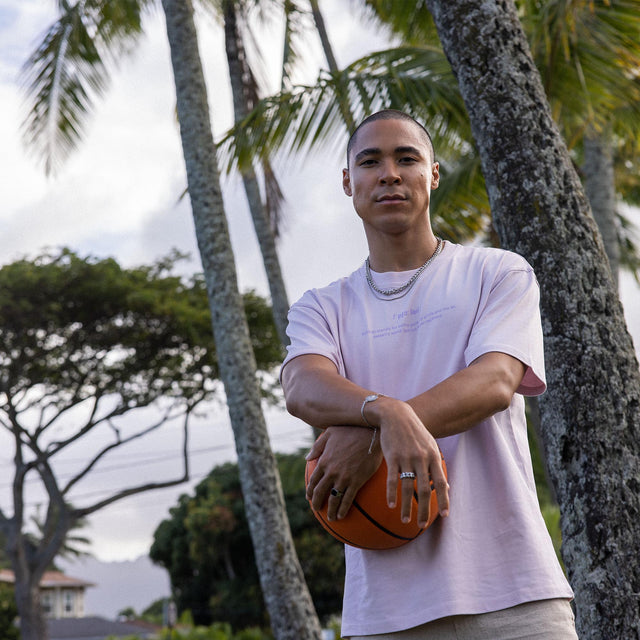 Mann mit Basketball, getragen mit PURELEI Schmuck, umgeben von Palmen im Freien.