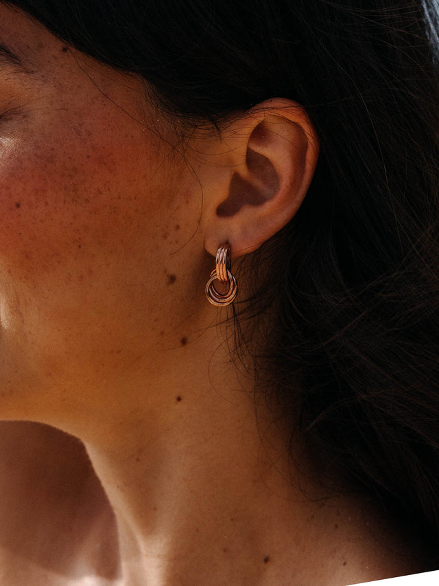 He Nui Ohrringe in 18K rosévergoldetem Edelstahl, verschlungene Ringe, getragen im warmen Tageslicht, PURELEI.