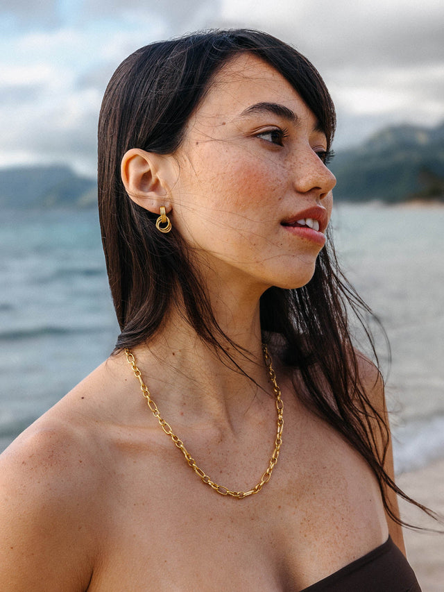 PURELEI He Nui Ohrringe in 18K Gold mit ineinander verschlungenen Ringen, getragen am Meer, elegant und selbstbewusst.