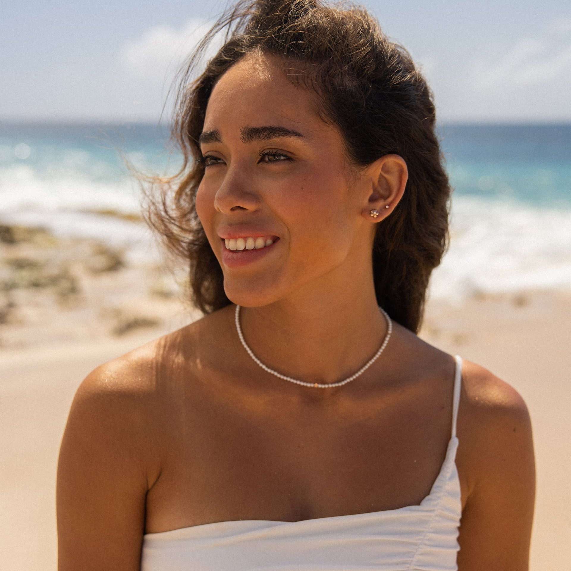 Zarte, allergenfreundliche Perlenkette von PURELEI, getragen am Strand mit tropischer Stimmung.