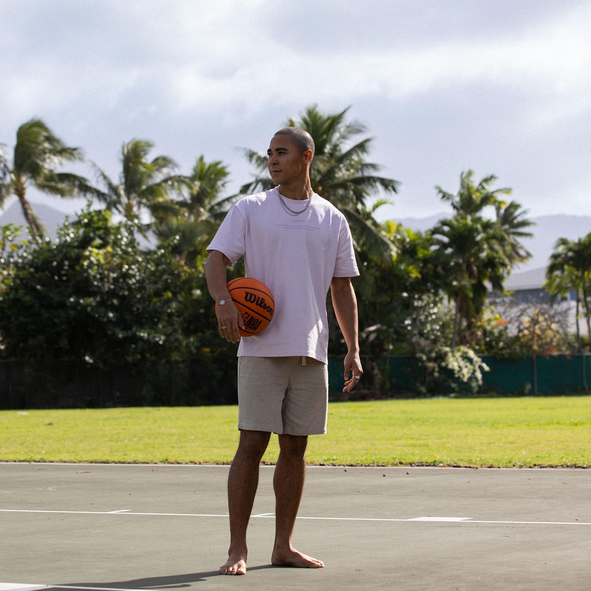 Mann in lässigem Outfit mit Basketball, umgeben von tropischer Natur – PURELEI Lifestyle.