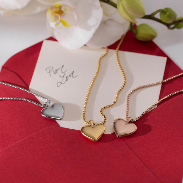 PURELEI Lovebird Kette in Gold, Silber und Roségold mit glänzendem Herzanhänger auf rotem Briefumschlag, elegant und feminin