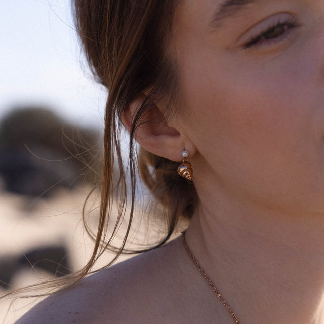 Roségoldene Muschel-Ohrringe mit Perle, getragen in sonniger Strandatmosphäre – PURELEI.