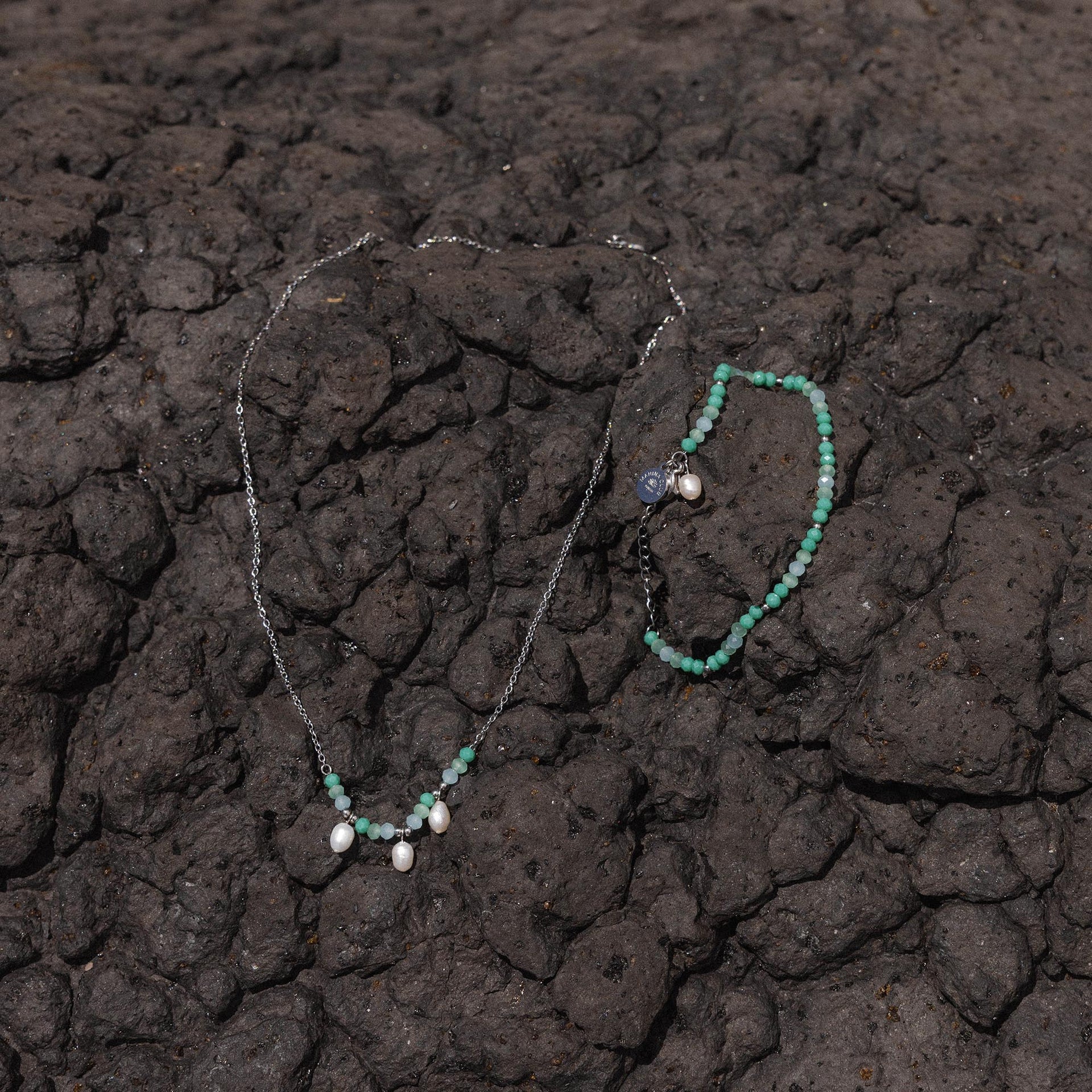 Silberne Kette und Armband mit runden Anhängern auf dunklem Lavagestein von PURELEI.