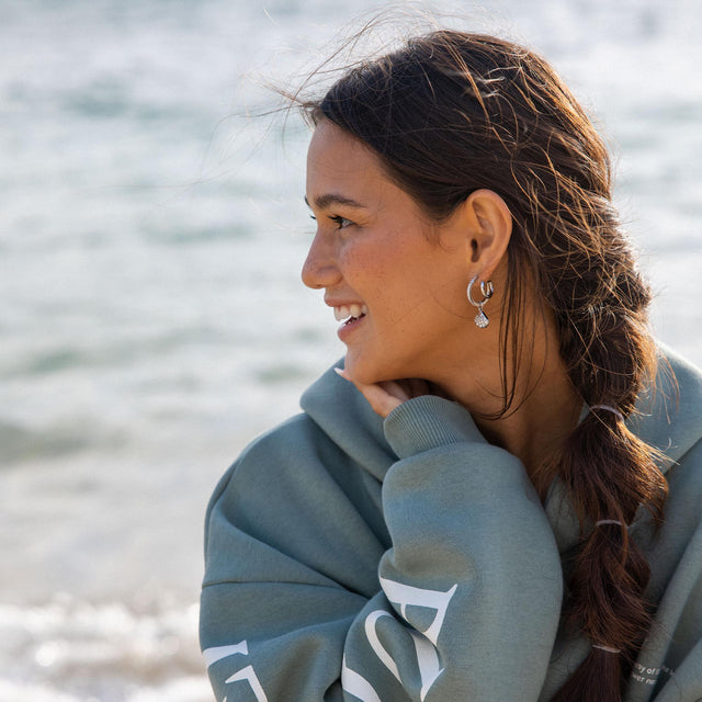 Silberne Ohrringe mit Muschel-Anhänger, getragen am Strand, PURELEI inspiriert.