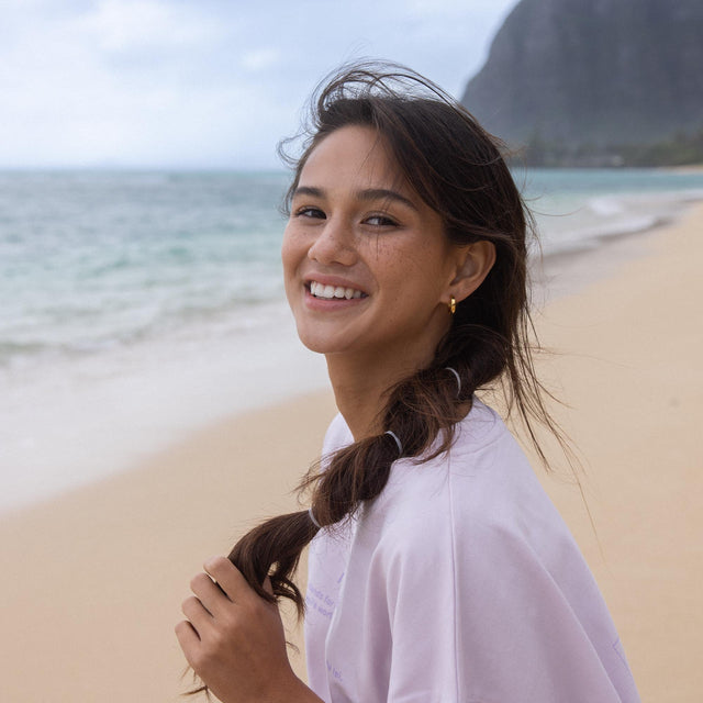 Lächelnde Frau am Strand mit PURELEI Schmuck, entspannte tropische Stimmung.