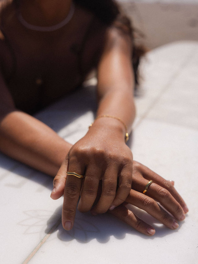 PURELEI Nakuna Ring in 18K Gold mit geschwungener Form, getragen an sonnengebräunter Hand, elegant und puristisch.