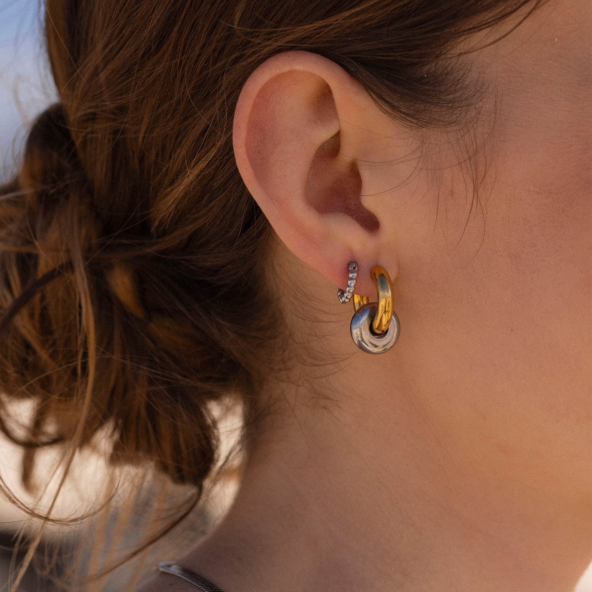 Silberne Creolen mit glänzendem Design, getragen am Ohr, von PURELEI.