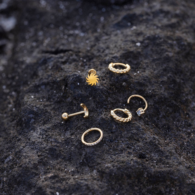 Goldene Ohrringe und Piercings auf dunklem Lavagestein, PURELEI inspiriert.