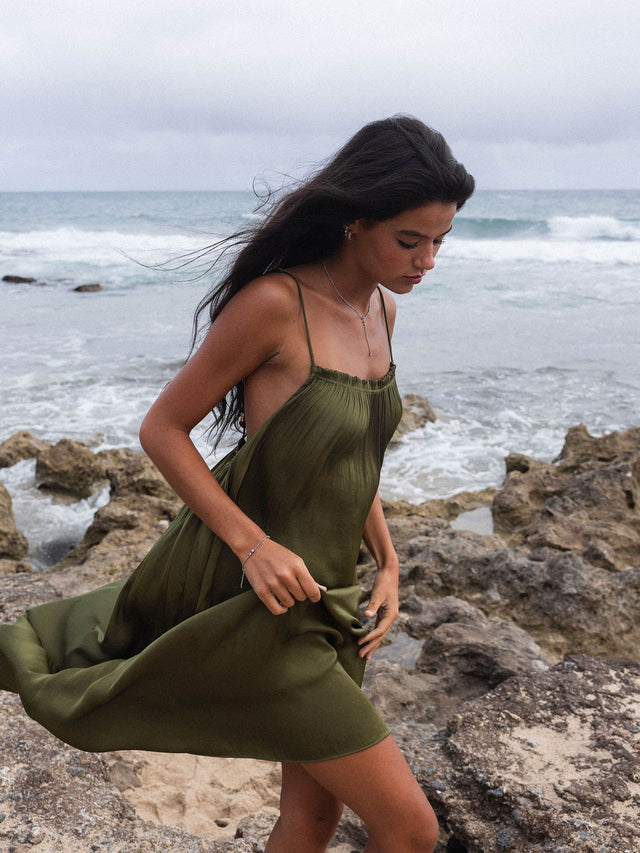 Braunes, luftiges Kleid am Strand mit PURELEI Schmuck, umgeben von Wellen und Felsen.