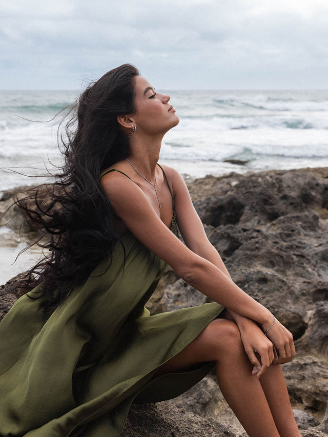 Frau mit langen Haaren, in einem fließenden Kleid, trägt PURELEI Schmuck am Strand.