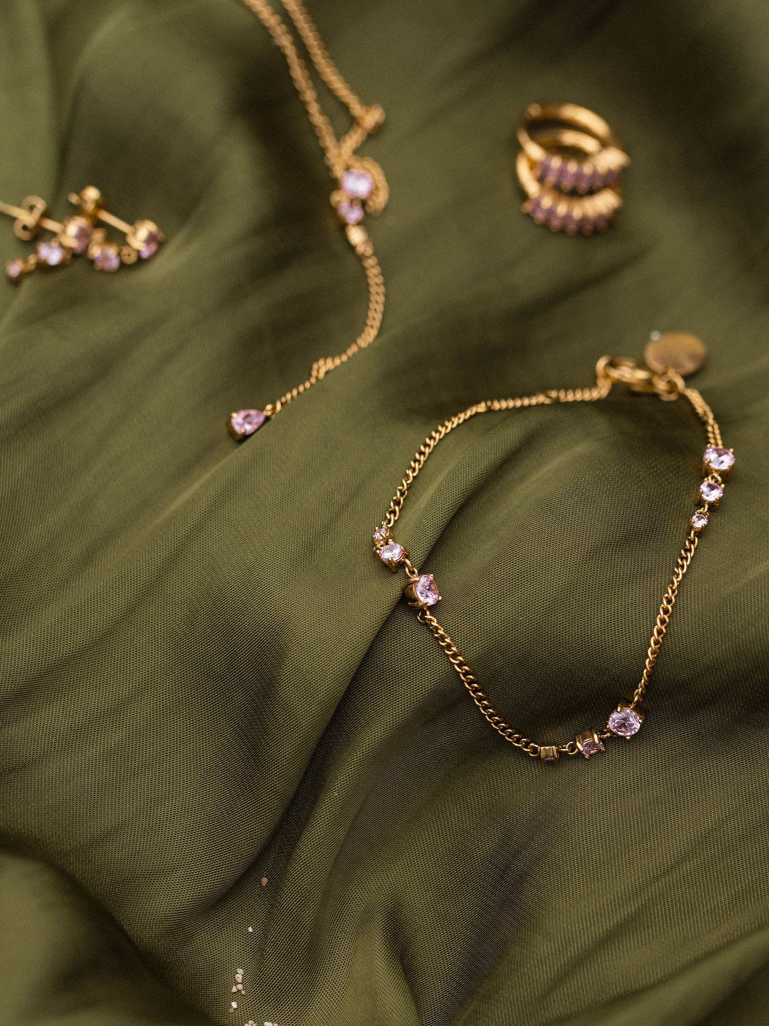 Goldene Schmuckstücke von PURELEI auf grünem Stoff, elegant und feminin.