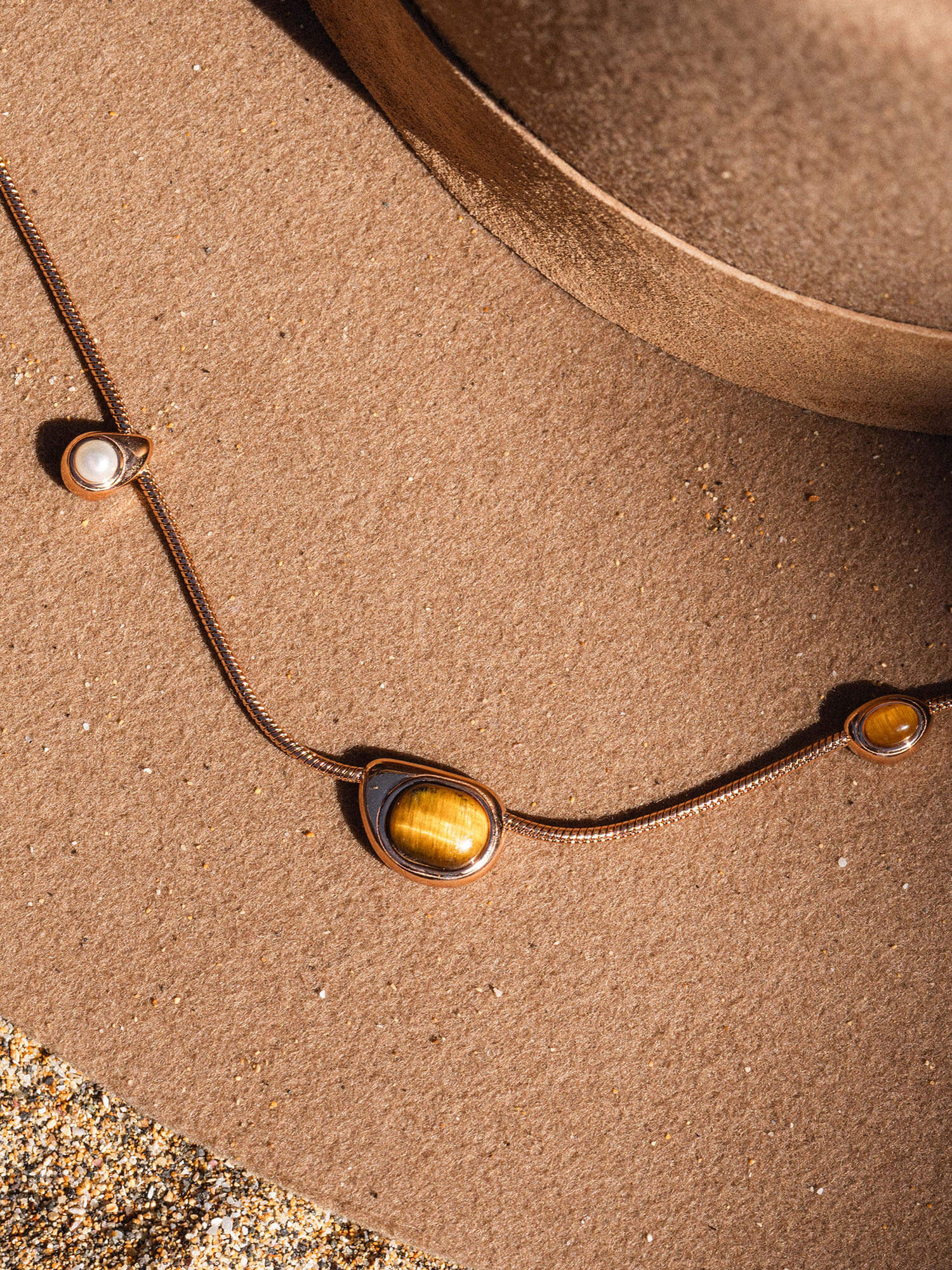 Goldene Kette mit zwei Anhängern auf sandigem Hintergrund, inspiriert von PURELEI.