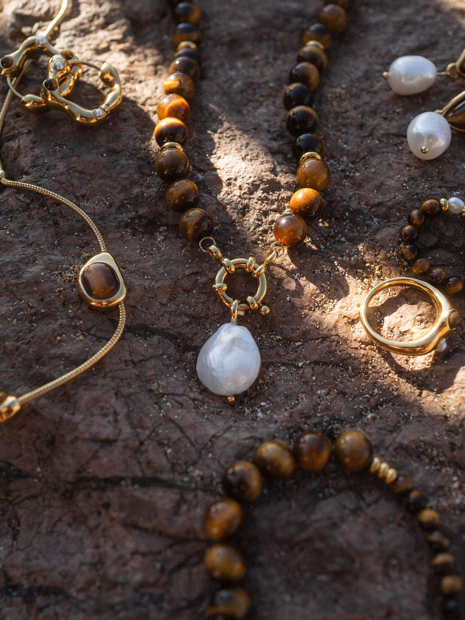 Goldene und braune Schmuckstücke von PURELEI auf dunklem Stein, elegant und natürlich.