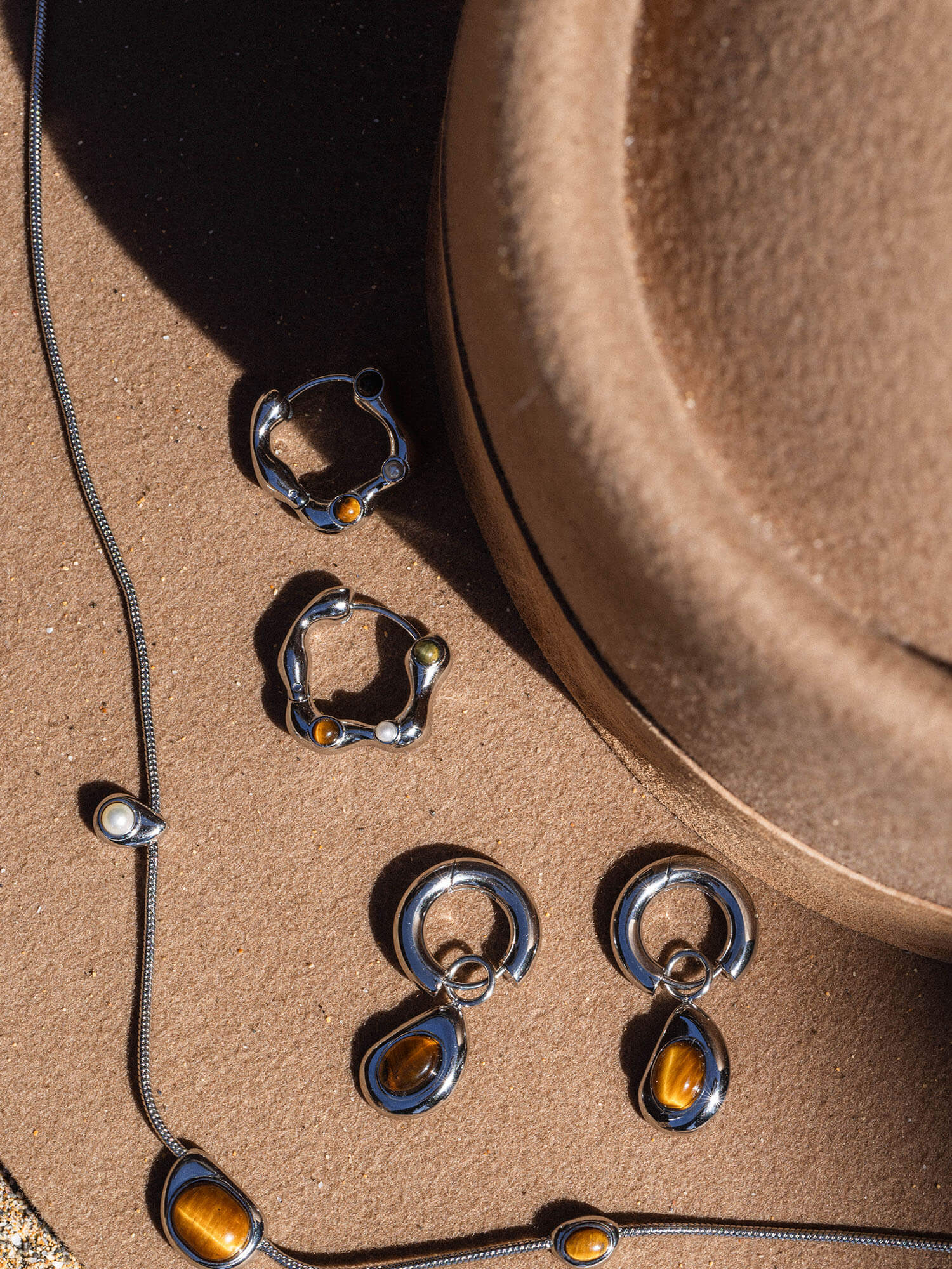 Silberne Ohrringe und Kette mit braunen Steinen, elegant auf einem Hut präsentiert – PURELEI.