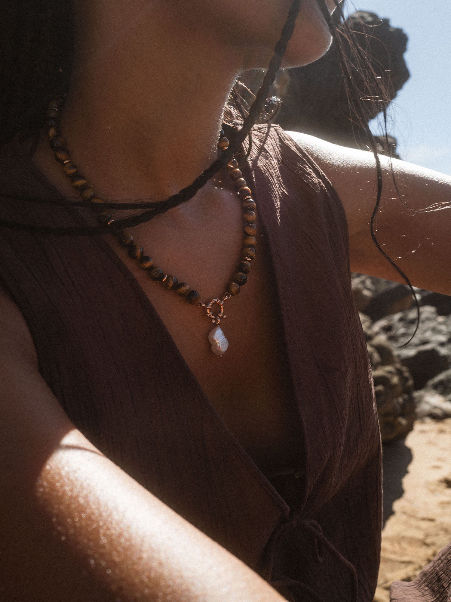 Braune Perlenkette mit Muschel-Anhänger, getragen in sonniger Strandatmosphäre – PURELEI.