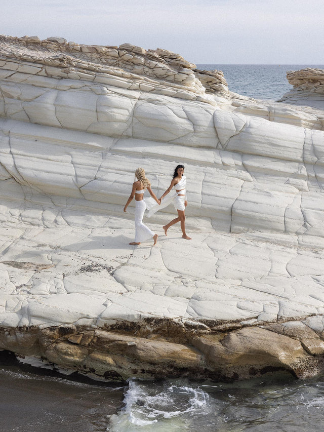 Capricorn Letter Charm in goldenem Edelstahl, elegant und feminin inszeniert vor Küstenfelsen von PURELEI.