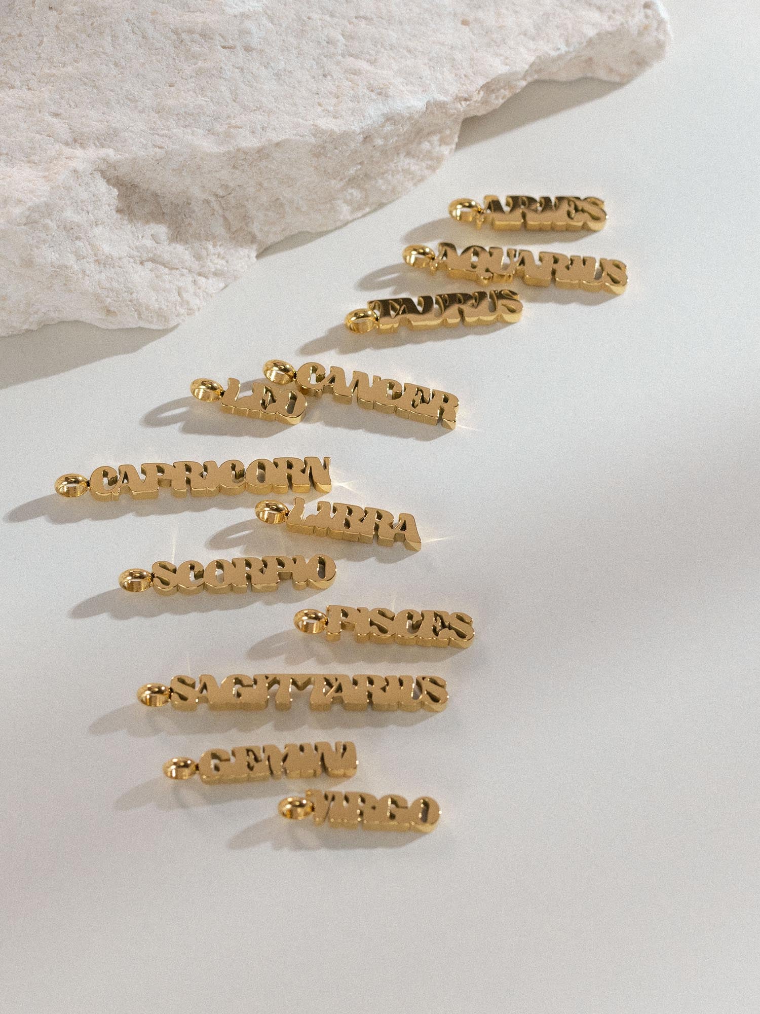 Goldener Aries Letter Charm aus Edelstahl, edel vergoldet, minimalistisch auf hellem Hintergrund, PURELEI.