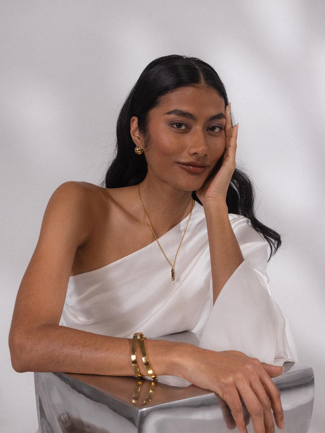 PURELEI Aries Letter Charm in vergoldetem Edelstahl, elegant und feminin getragen mit weißer Seidenbluse